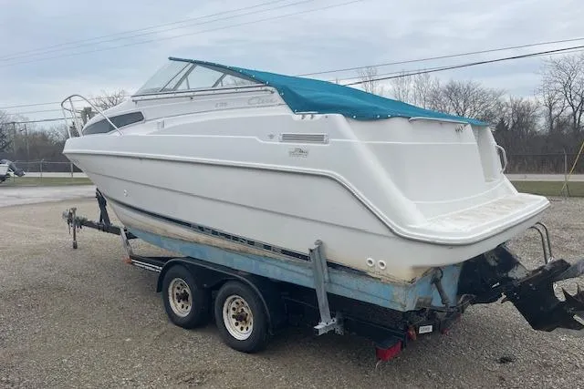 Slide: The Image of 1997 Bayliner 2355 boat on trailer, white hull, blue cover, parked outdoors. - 2
