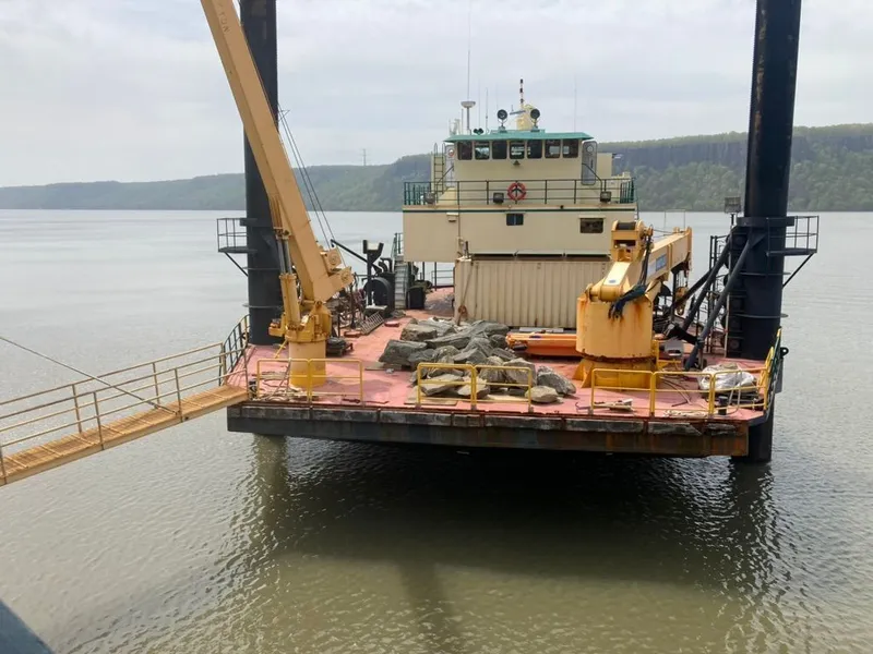 Slide: The Image of Custom 1981 lift boat with cranes on calm water, docked near a forested shoreline. - 2