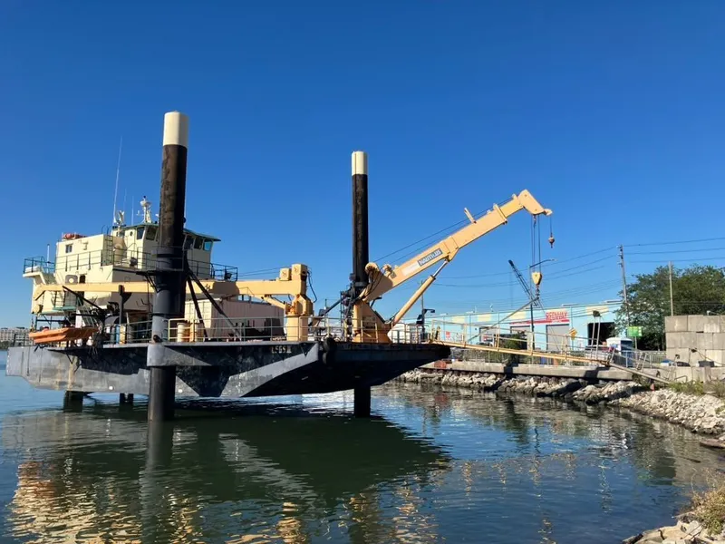Slide: The Image of Custom 1981 lift boat with crane docked by rocky shoreline under clear blue sky. - 3