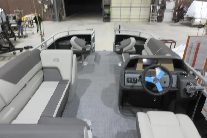 Slide: The Image of 2026 Sun Tracker Fishin' Barge 20 DLX interior with seating and steering console in a warehouse. - 3
