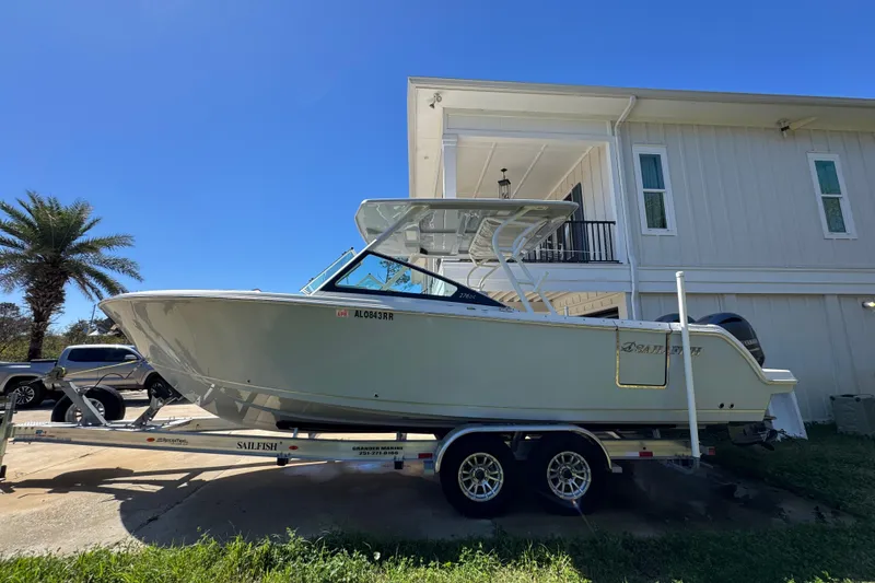 The Image of 2022 Sailfish 276 DC boat on trailer beside a house under clear blue sky. - 1