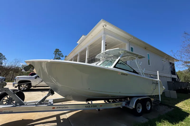 Slide: The Image of 2022 Sailfish 276 DC boat on trailer, parked beside a house under clear blue sky. - 3