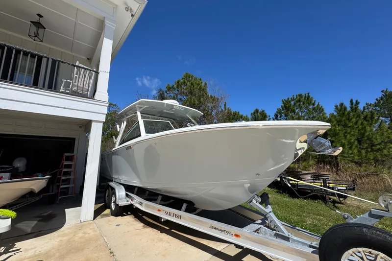 Slide: The Image of 2022 Sailfish 276 DC boat on trailer beside house under clear blue sky. - 8