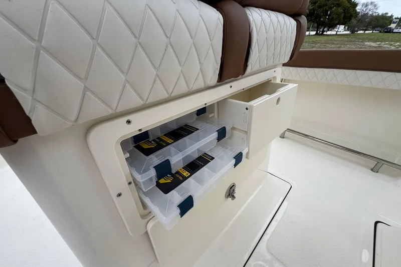 Slide: The Image of 2026 Pioneer 202 Sportfish boat storage compartment with tackle boxes and cushioned seating. - 13