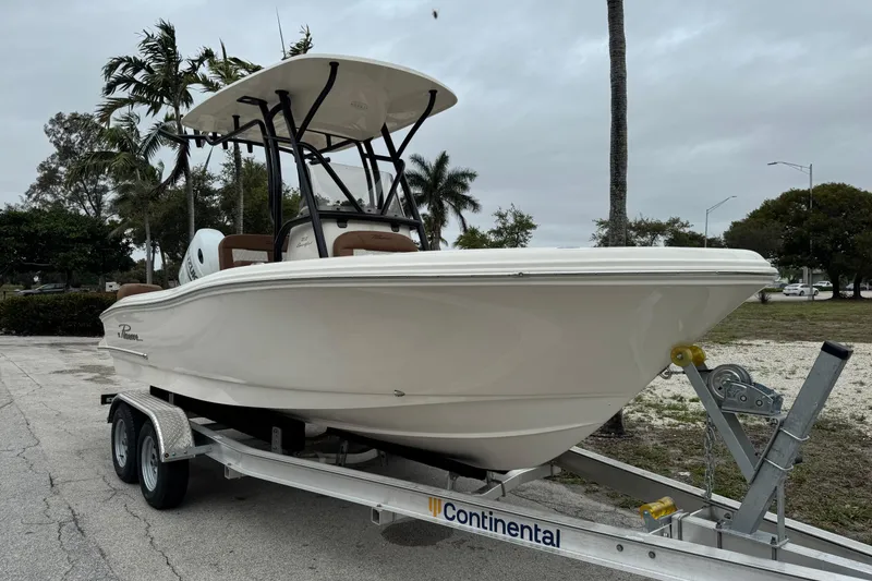 Slide: The Image of 2026 Pioneer 202 Sportfish boat on trailer, parked outdoors with palm trees in background. - 2