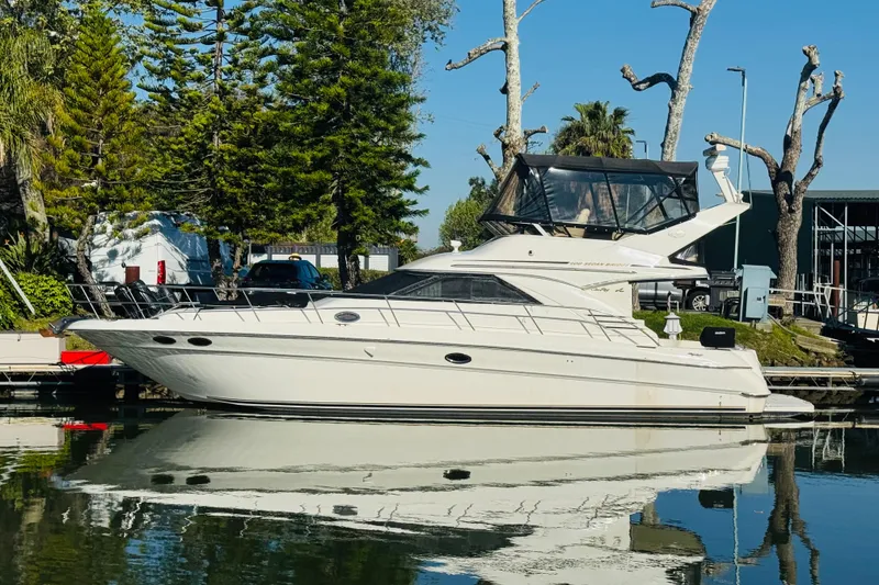 The Image of 2000 Sea Ray 400 Sedan Bridge yacht docked by trees, reflecting on calm water. - 0