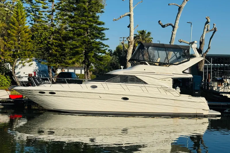 Slide: The Image of 2000 Sea Ray 400 Sedan Bridge yacht docked by trees, reflecting on calm water. - 3