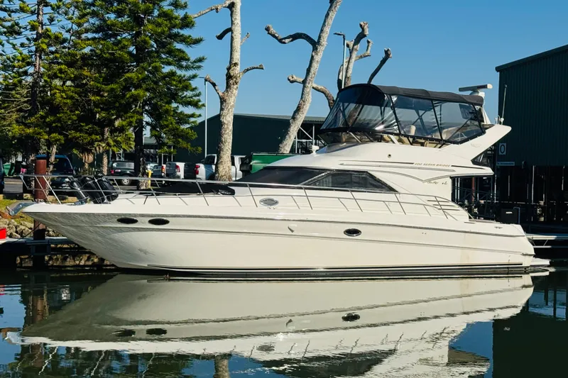 Slide: The Image of 2000 Sea Ray 400 Sedan Bridge yacht docked, reflecting on calm water, surrounded by trees. - 4