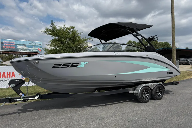 The Image of 2026 Yamaha Boats 255XD on trailer, sleek design, gray with teal accents, under cloudy sky. - 1