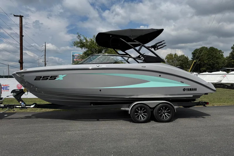 Slide: The Image of 2026 Yamaha Boats 255XD on trailer, sleek gray design with teal accents, under cloudy sky. - 2