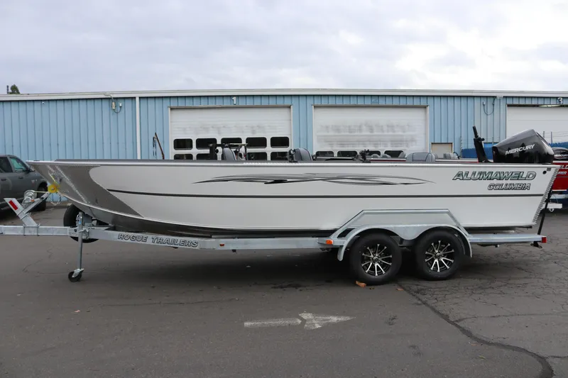 The Image of 2026 Alumaweld Columbia 23 boat on Rogue trailer, parked outside a blue building. - 1