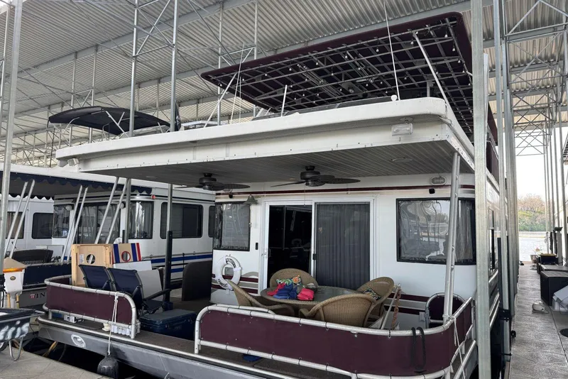 Slide: The Image of 1999 Sumerset 18 x 78 houseboat docked, featuring outdoor seating and covered upper deck. - 2