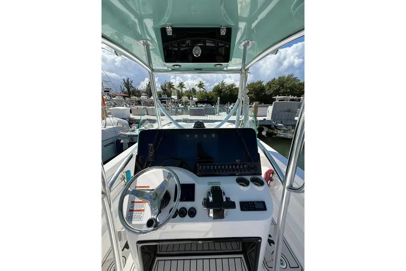 Slide: The Image of 2024 TwinVee 240 CFX CC boat console with steering wheel and controls, docked at marina. - 7