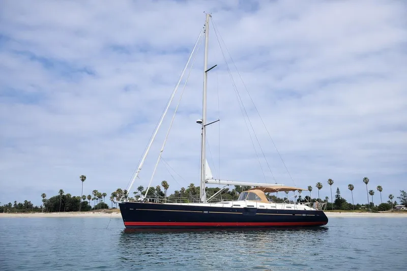 The Image of 2006 Beneteau Oceanis 523 sailboat anchored near a tropical shoreline under a cloudy sky. - 0