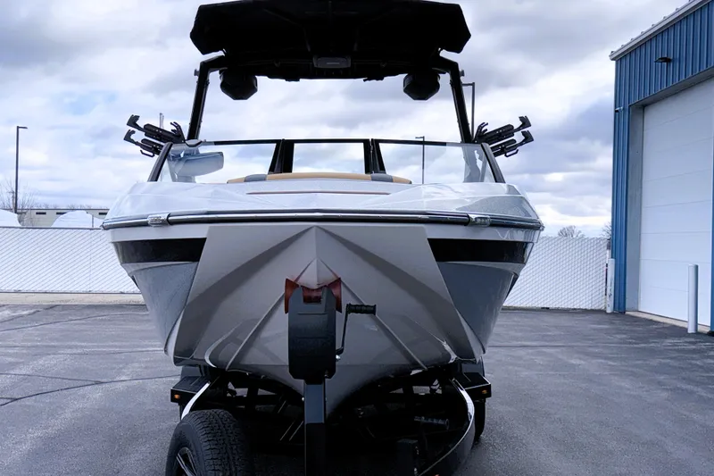 Slide: The Image of 2023 Tigé 23ZX boat on trailer, front view, parked near blue building. - 2