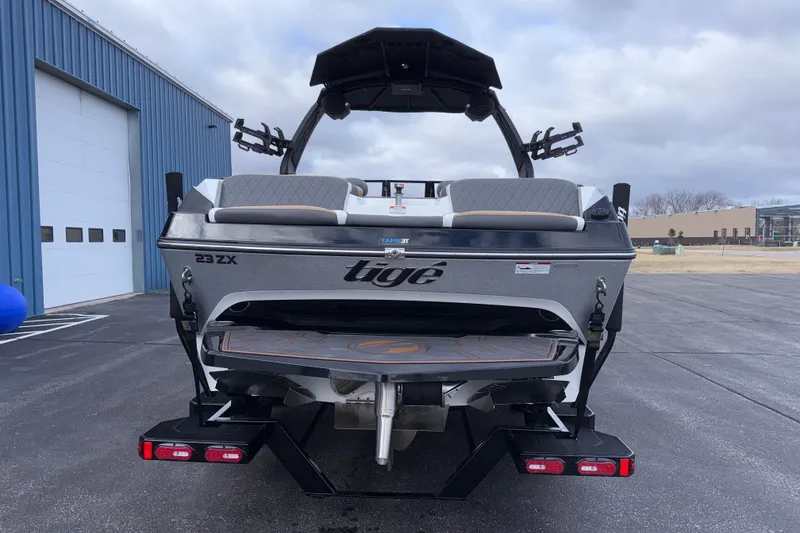 Slide: The Image of 2023 Tigé 23ZX boat rear view, parked near a blue building under cloudy skies. - 5