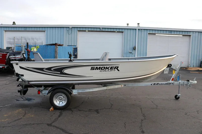 The Image of 2026 Smoker Craft Alaskan 15 boat on trailer, parked outside industrial building. - 1