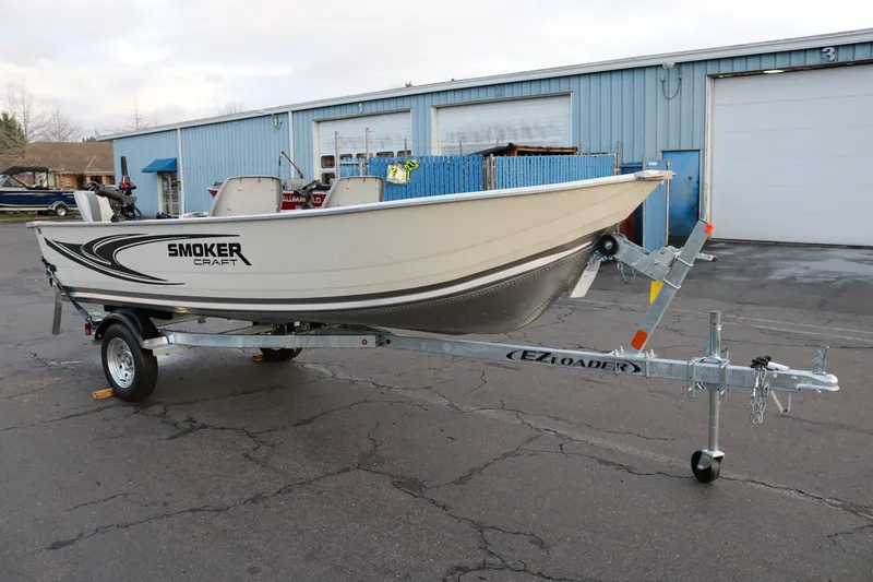 Slide: The Image of 2026 Smoker Craft Alaskan 15 boat on trailer outside a blue warehouse. - 2