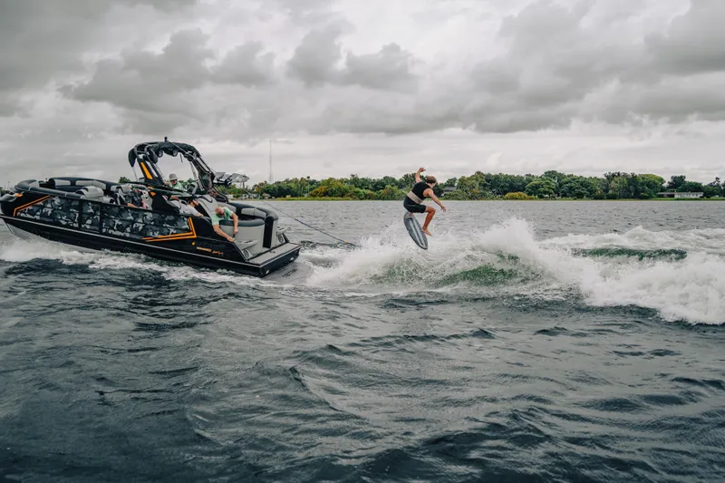 Slide: The Image of 2024 Montara 23 Surf Boss 2.0 CW towing a wakeboarder on a lake under cloudy skies. - 1
