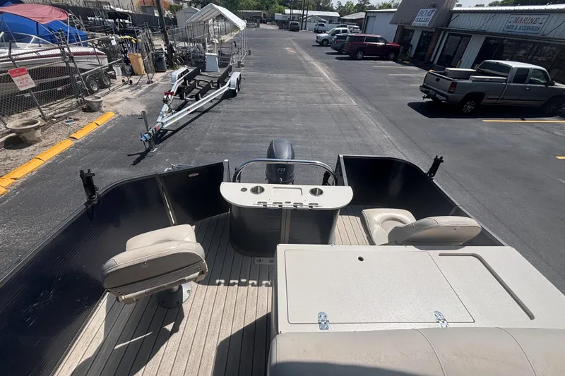 Slide: The Image of 2015 Manitou 20 Oasis Angler pontoon boat interior with seating and console, parked outdoors. - 15