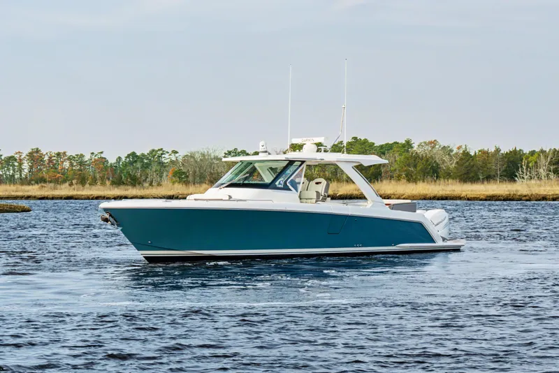 Slide: The Image of 2022 Tiara 38LS boat cruising on a calm lake with forested shoreline. - 5