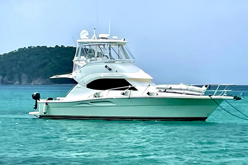 The Image of 2005 Riviera 37 Flybridge yacht anchored in turquoise waters near a lush island. - 0