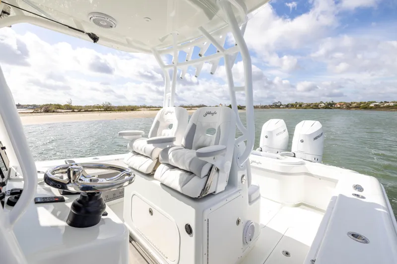 Slide: The Image of 2014 Yellowfin 32 Offshore boat interior with dual engines, steering wheel, and seating near shoreline. - 16