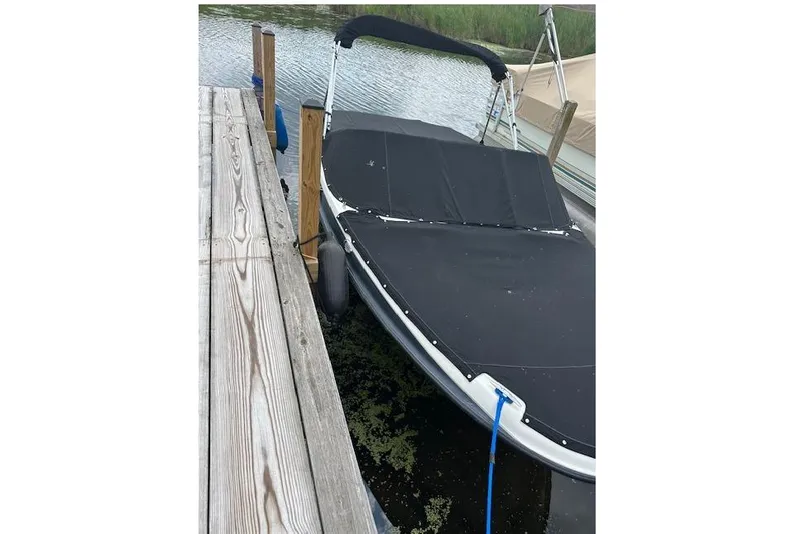Slide: The Image of 2011 Bayliner 185 boat docked with black cover, calm water background. - 7