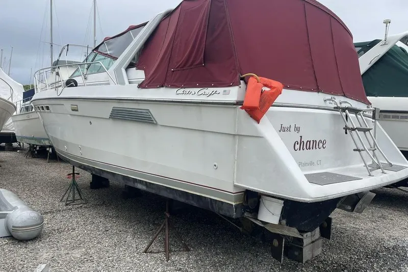 Slide: The Image of 1987 Chris-Craft 332 Amerosport boat with maroon cover, docked on gravel. - 24