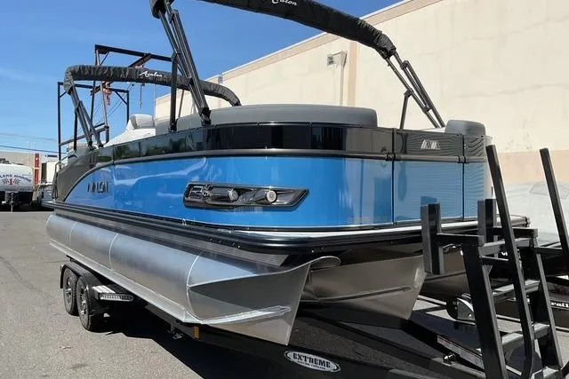 Slide: The Image of 2025 Avalon LSZ Quad Lounge Shift pontoon boat on trailer, blue and black design. - 2