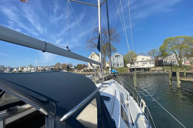 Slide: The Image of 2006 Hunter 41 Deck Salon sailboat docked near waterfront homes under clear blue sky. - 32