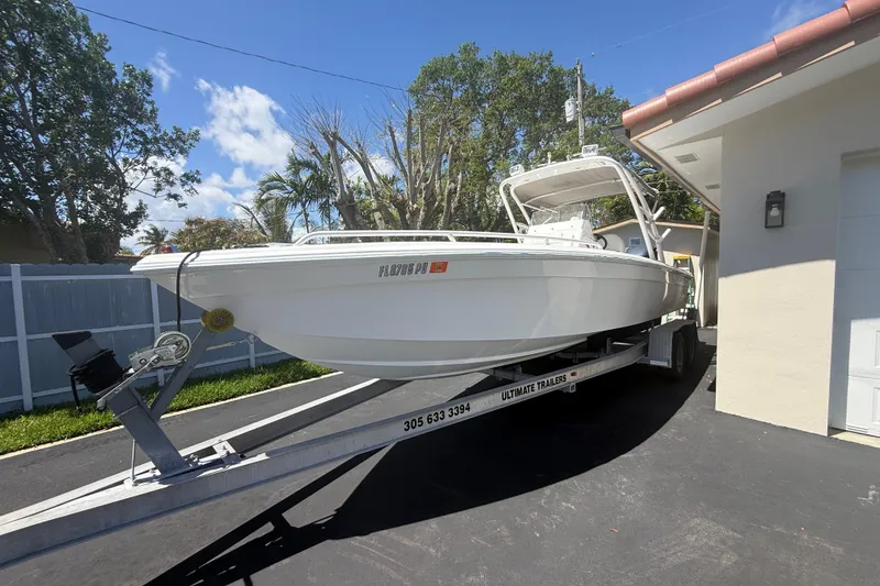 Slide: The Image of White 2015 Concept 27 boat on trailer in driveway, surrounded by trees and blue sky. - 129