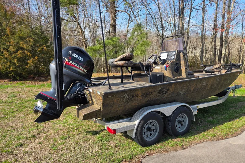 Slide: The Image of 2019 G3 Bay 20 DLX Camo boat with Yamaha engine on trailer in wooded area. - 2