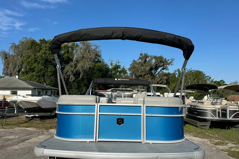 Slide: The Image of 2026 Sweetwater EX 2286 SFLX pontoon boat with blue exterior and canopy, parked outdoors. - 2