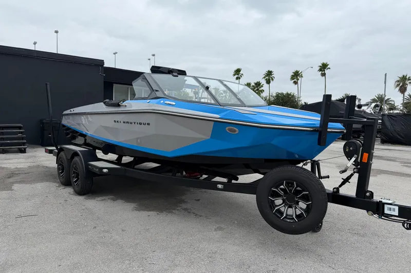 The Image of 2026 Nautique Ski Nautique boat on trailer, blue and gray design, parked outdoors. - 1