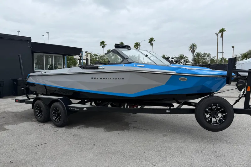 Slide: The Image of 2026 Nautique Ski Nautique boat in blue and gray on a trailer, parked outdoors. - 3