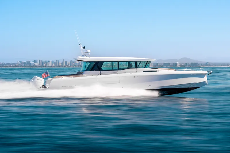 The Image of 2026 Axopar 45 XC Cross Cabin cruising swiftly on open water, city skyline in background. - 0