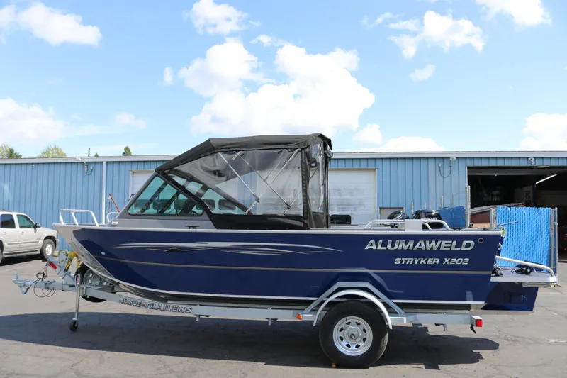 Slide: The Image of 2025 Alumaweld Stryker X202 boat on trailer, parked outside a blue building. - 5