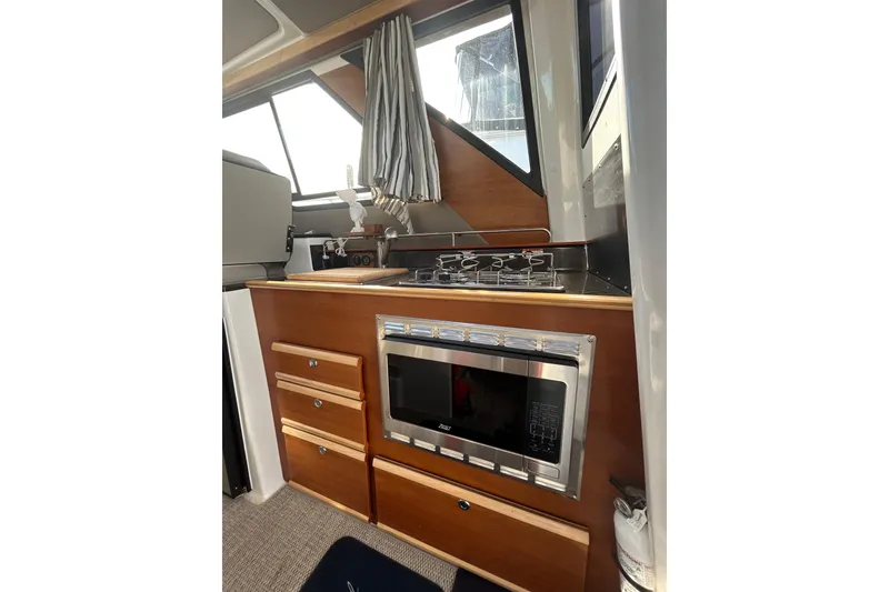 Slide: The Image of 2024 Cutwater C-288 Coupe interior kitchen with stove, microwave, and wooden cabinetry. - 16