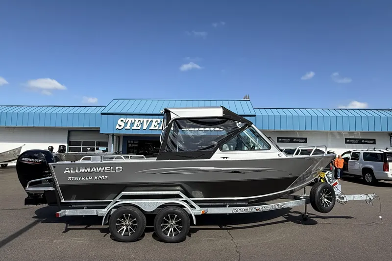 The Image of 2025 Alumaweld Stryker X202 boat on trailer, parked outside dealership under clear blue sky. - 1