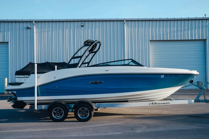 Slide: The Image of 2023 Sea Ray SPX 230 boat on trailer, parked outside a warehouse. - 1