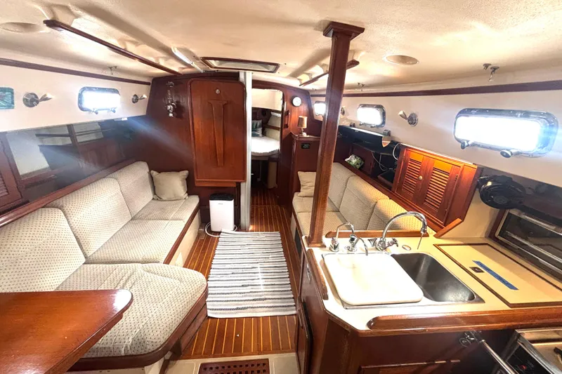 Slide: The Image of Interior of a 1995 Island Packet 37 sailboat, featuring cozy seating and a compact kitchen. - 5