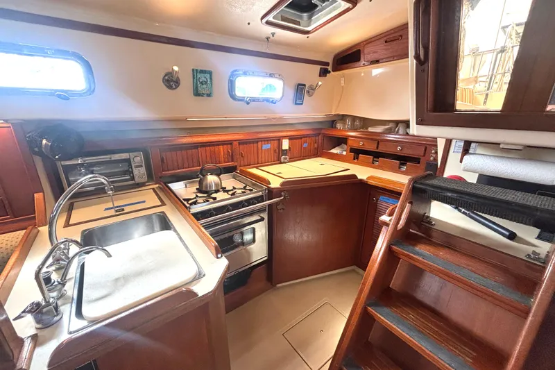 Slide: The Image of Cozy 1995 Island Packet 37 yacht kitchen with stove, sink, and wooden cabinetry. - 9