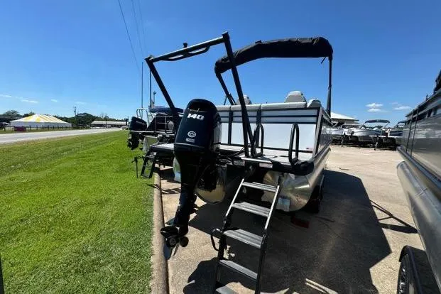 Slide: The Image of 2024 Viaggio Lago X22Q pontoon boat with outboard motor and ladder, parked on pavement. - 2