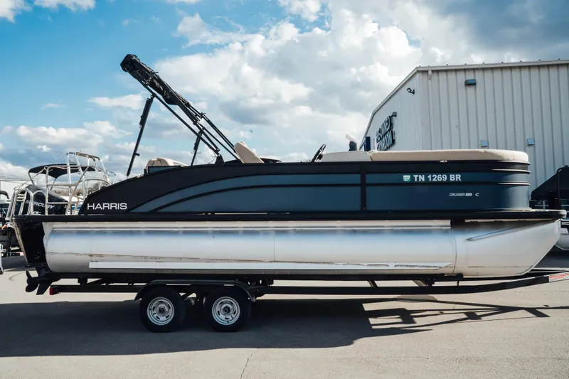 The Image of 2024 Harris Cruiser 230 pontoon boat on trailer, parked outdoors under a cloudy sky. - 0