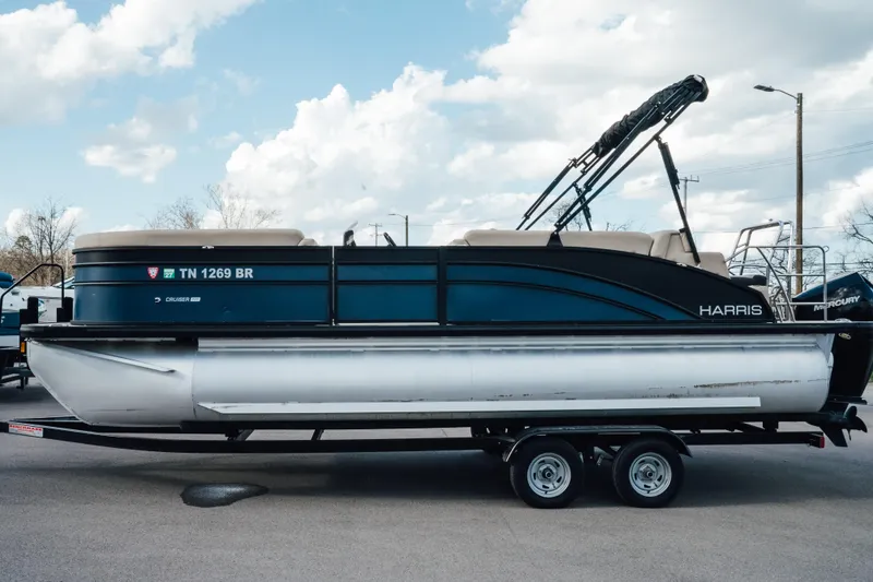 Slide: The Image of 2024 Harris Cruiser 230 pontoon boat on trailer under a cloudy sky. - 1