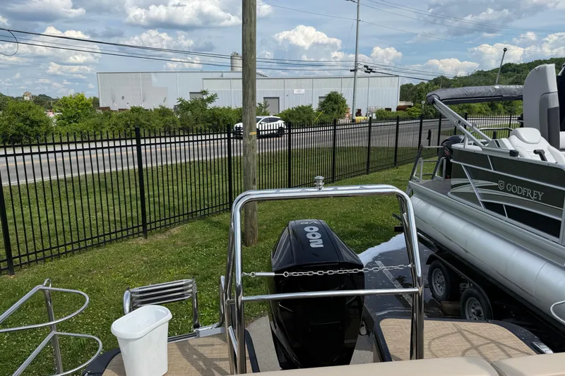 Slide: The Image of 2024 Harris Cruiser 230 boat with outboard motor, parked near a fence and road. - 5