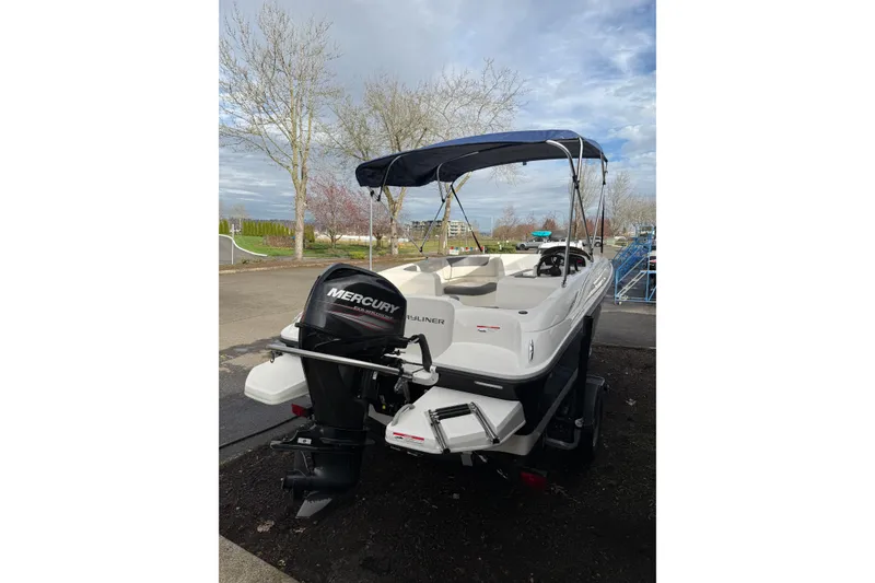 Slide: The Image of 2019 Bayliner Element E16 boat with Mercury engine, parked outdoors under cloudy sky. - 2