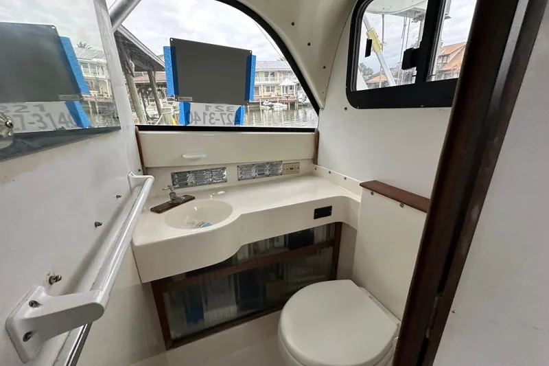 Slide: The Image of 1975 Bertram 31 boat bathroom interior with sink and toilet, dock view outside window. - 36