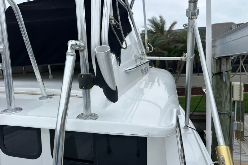 Slide: The Image of 1975 Bertram 31 boat with metal railings and fishing rod holder, docked near palm trees. - 48